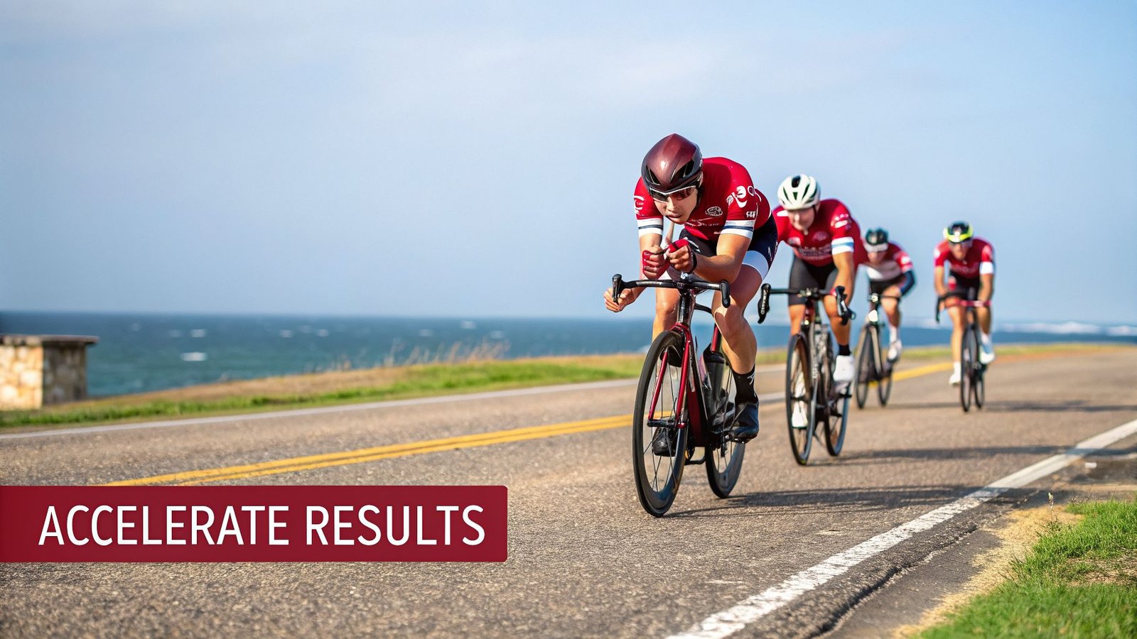 Four cyclists in red jerseys race along a scenic coastal road next to the ocean.